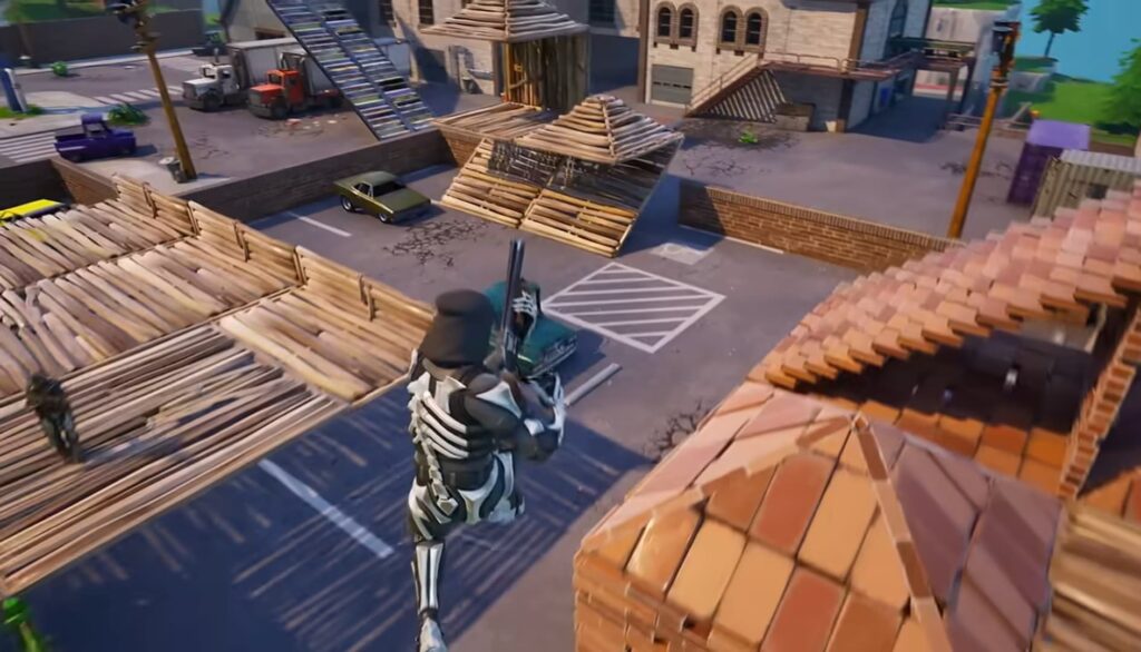 A screenshot from the game Fortnite, featuring a character in a skeleton skin jumping over a street in a built-up area with other players and wooden structures