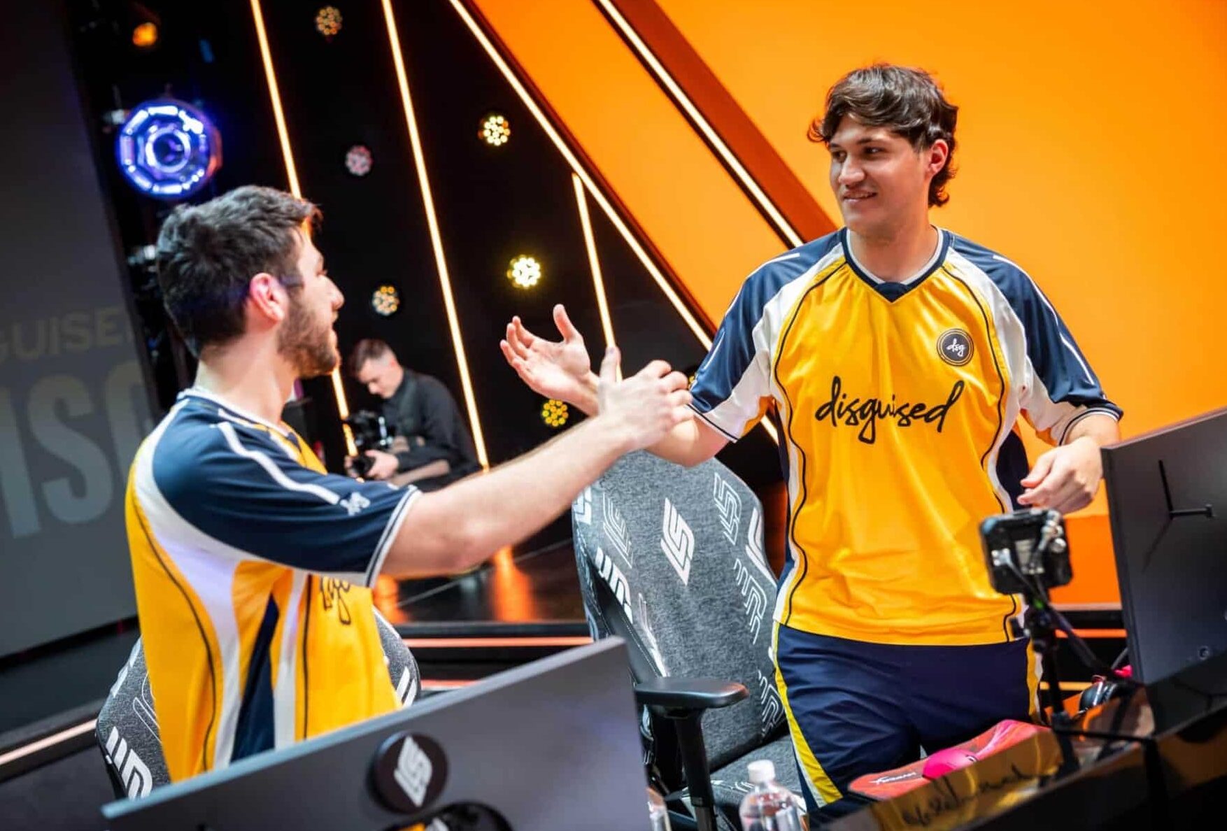 Zwei männliche E-Sport-Spieler tragen gelbe und blaue Trikots mit dem Wort "verkleidet" Die darauf geschriebenen Figuren interagieren nach einem Spiel fröhlich auf einer E-Sport-Bühne