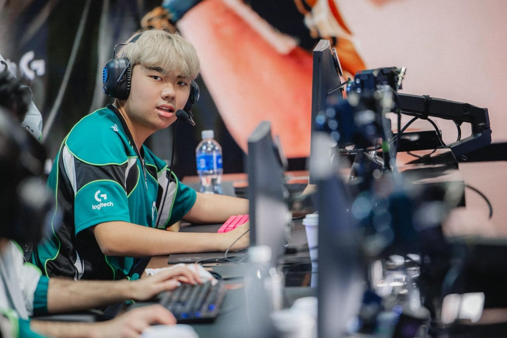 Ein junger männlicher E-Sport-Spieler, der ein blaugrünes Logitech-G-Trikot und ein Gaming-Headset trägt, sitzt während eines Wettkampfs an einem Computer