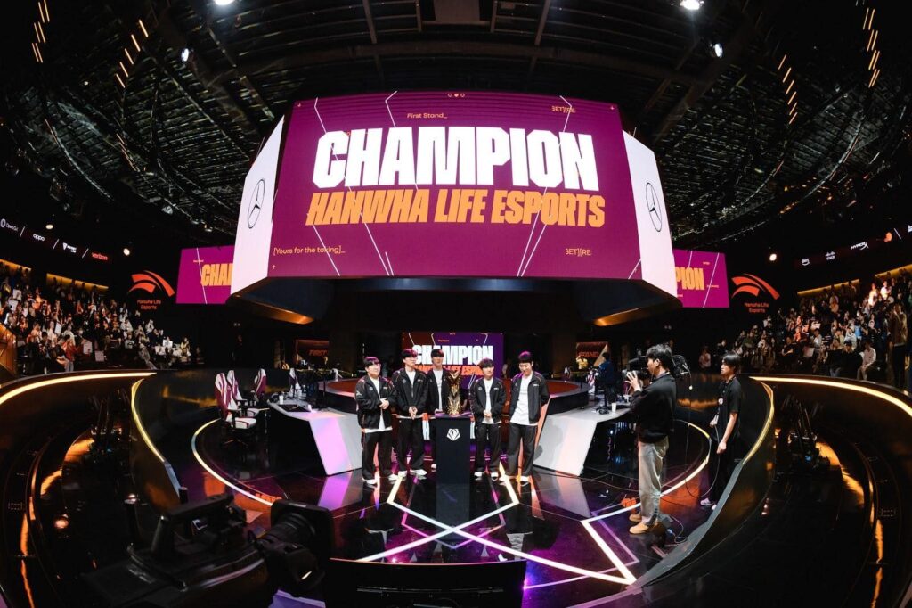 Fünf professionelle eSportler stehen zusammen auf einer Bühne und halten eine Trophäe und einen LCK-Wimpel in der Hand, während Konfetti regnet. Auf einem großen Bildschirm dahinter werden die Worte angezeigt "CHAMPION HANWHA LIFE ESPORTS"