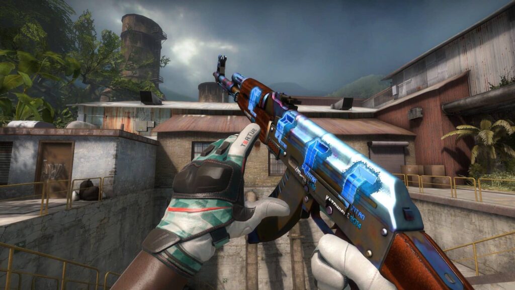 A first-person view from the video game Counter-Strike shows a character holding an AK-47 assault rifle with a distinctive blue "Case Hardened" skin and "Titan 2014" stickers, in an outdoor map environment