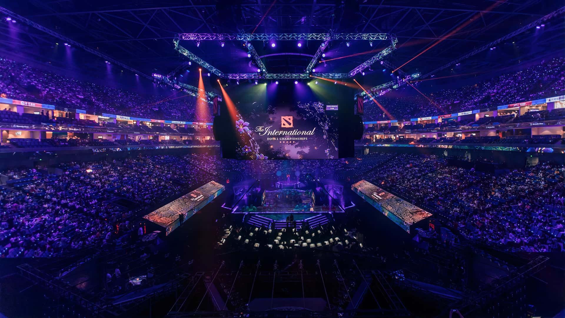 Eine weite Luftaufnahme der überfüllten Mercedes-Benz Arena in Shanghai, beleuchtet von leuchtend blauer und violetter Bühnenbeleuchtung, während der Dota 2 The International 2019 eSports-Meisterschaftsveranstaltung