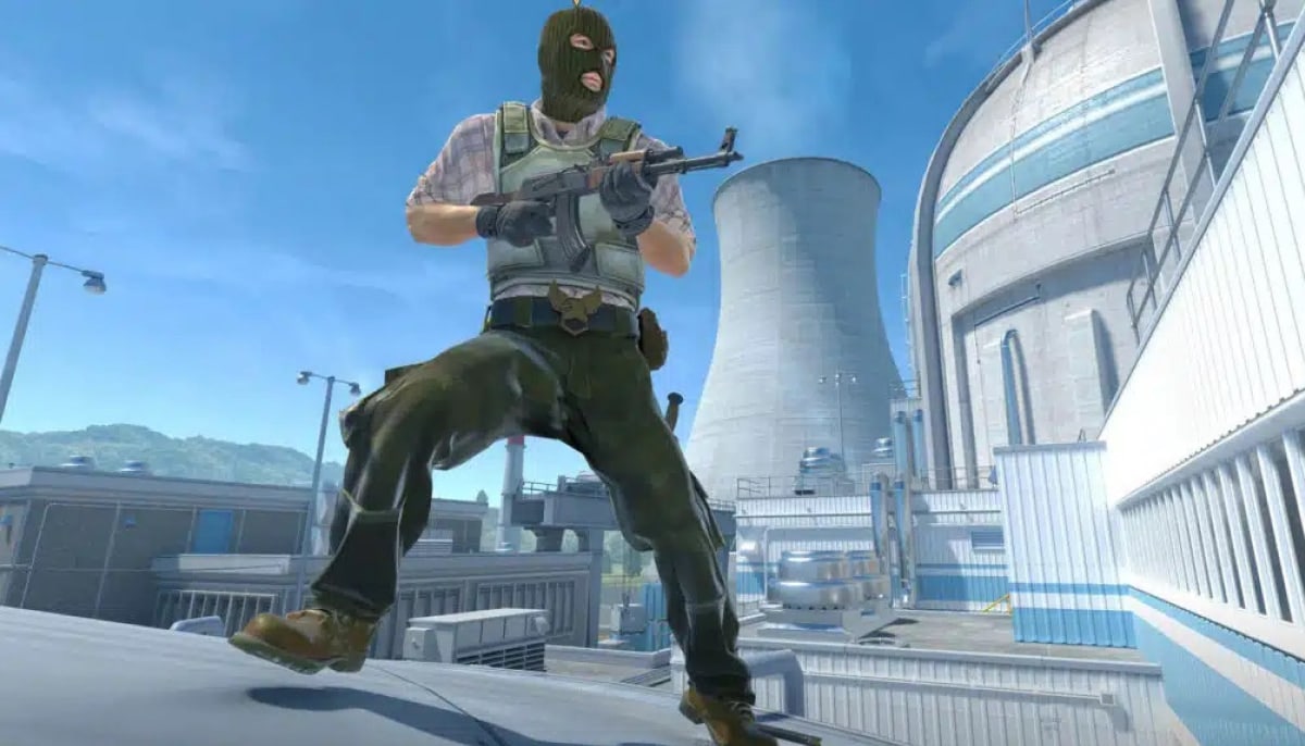 A video game screenshot of a Counter-Strike terrorist character wearing a green balaclava and tactical gear, crouching dynamically on a rooftop while holding a rifle